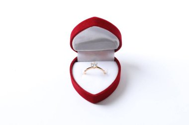 Güzel, parlak altın bir nişan yüzüğü. Beyaz arka planda izole edilmiş çiçekli kırmızı kadife bir kutuda büyük bir elmas mücevher var.