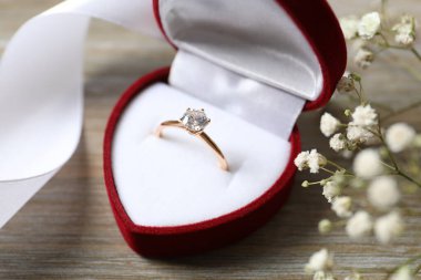 Güzel, parlak, altın bir nişan yüzüğü. Büyük elmas değerli taşlı. Ahşap arka planda çiçekler olan kırmızı kadife bir kutuda.