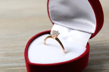 Tahta zemin üzerinde kırmızı kadife bir kutuda büyük elmas mücevher taşıyla güzel, parlak altın bir nişan yüzüğü.