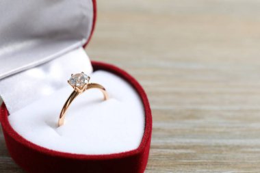 Tahta zemin üzerinde kırmızı kadife bir kutuda büyük elmas mücevher taşıyla güzel, parlak altın bir nişan yüzüğü.