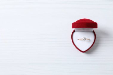 Tahta zemin üzerinde kırmızı kadife bir kutuda büyük elmas mücevher taşıyla güzel, parlak altın bir nişan yüzüğü.