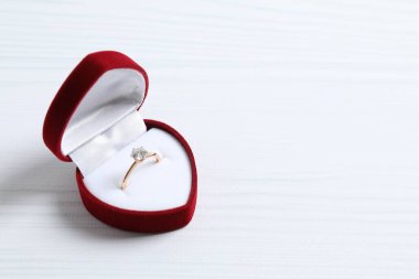 Tahta zemin üzerinde kırmızı kadife bir kutuda büyük elmas mücevher taşıyla güzel, parlak altın bir nişan yüzüğü.