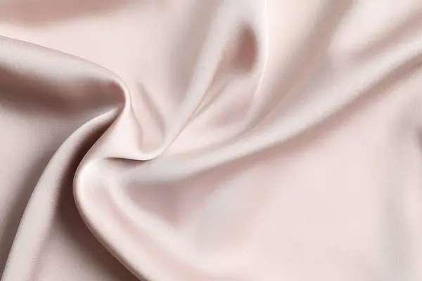 Beige silk satin. Shiny smooth fabric. Soft folds. Luxury background with space for design.