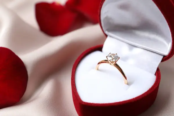 美丽的金光闪闪的订婚戒指 丝织品上镶嵌着巨大的钻石宝石 镶嵌在一个华丽的红色天鹅绒盒中 免版税图库图片