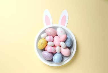 Paskalya dekoru konsepti. Renkli yumurtaların renkli bir tabakta, pastel arka planda tavşan kulaklı bir fotoğrafı.
