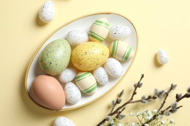 Paskalya dekoru konsepti. Pastel arka planda bir tabakta renkli yumurtaların en üstteki görüntüsü