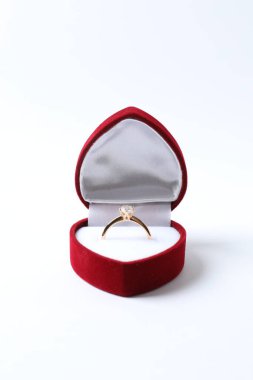 Güzel, parlak, altın bir nişan yüzüğü. Beyaz arka planda kırmızı kadife bir kutuda büyük elmas bir mücevher var. 