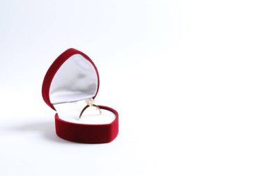 Güzel, parlak, altın bir nişan yüzüğü. Beyaz arka planda kırmızı kadife bir kutuda büyük elmas bir mücevher var. 