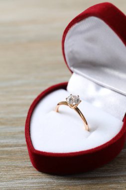 Zengin kırmızı kadife bir kutuda büyük elmas taşlı güzel, parlak altın bir nişan yüzüğü. 