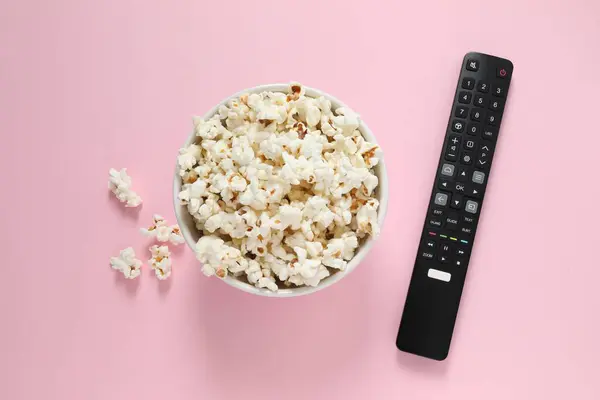 Popcorn and TV remote controller on color background
