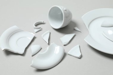 Beyaz bardak ve tabak gri arka planda kırılmış. 