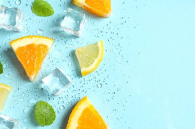 Nane yapraklarının üst görüntüsü, portakal, limon ve buz dilimleri ve pastel mavi arka planda su damlaları. 