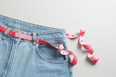Sağlıklı yaşam tarzı ve diyet konsepti. Gri arka planda kemer yerine ölçü bandı olan mavi kot pantolon.