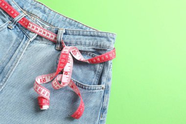 Sağlıklı yaşam tarzı ve diyet konsepti. Renkli bir arka planda kemer yerine ölçü bandı olan mavi kot pantolon.