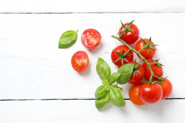 Bir demet taze kırmızı domates ve ahşap arka planda fesleğen.