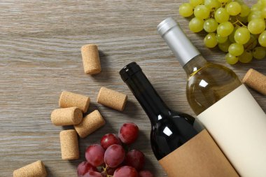 İki şişe kırmızı beyaz şarap ve ahşap arka planda üzümler