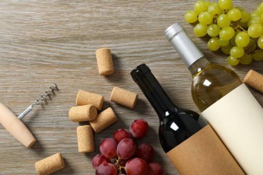 İki şişe kırmızı beyaz şarap ve ahşap arka planda üzümler