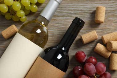 İki şişe kırmızı beyaz şarap ve ahşap arka planda üzümler