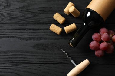 Üzümlü bir şişe kırmızı şarap, ahşap arka planda tirbuşon ve mantar.