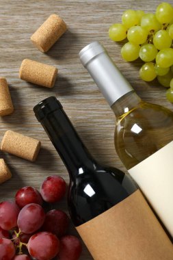 İki şişe kırmızı beyaz şarap ve ahşap arka planda üzümler