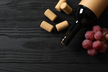 Ahşap arka planda üzüm ve mantarlı bir şişe kırmızı şarap.