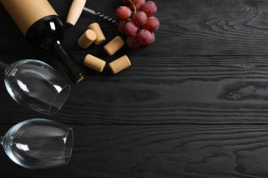 Ahşap zemin üzerinde üzüm ve bardak bulunan bir şişe kırmızı şarap.