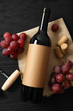 Ahşap arka planda üzüm ve mantarlı bir şişe kırmızı şarap.