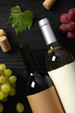 Ahşap arka planda üzüm ve mantarlı bir şişe kırmızı ve beyaz şarap.