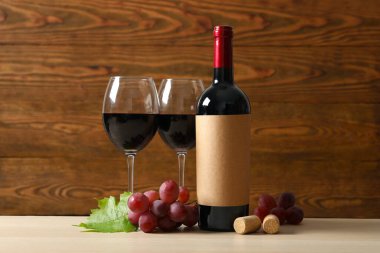 Ahşap zemin üzerinde üzüm ve bardak bulunan bir şişe kırmızı şarap.