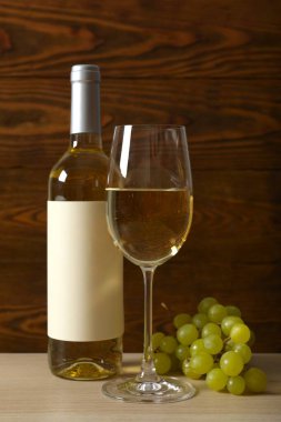 Üzümlü bir şişe beyaz şarap ve ahşap zemin üzerinde cam.