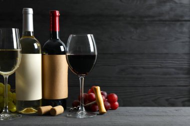 İki şişe kırmızı beyaz şarap ve tahta zemin üzerinde üzüm ve bardak.