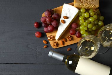 Tahta arka planda çeşitli peynirler, üzümler, fındıklar ve beyaz şarap.