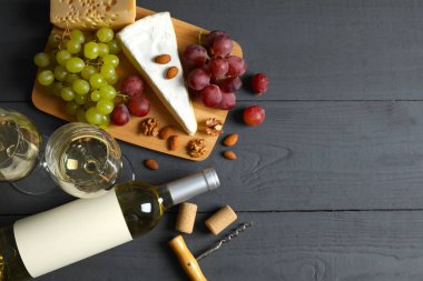 Tahta arka planda çeşitli peynirler, üzümler, fındıklar ve beyaz şarap.
