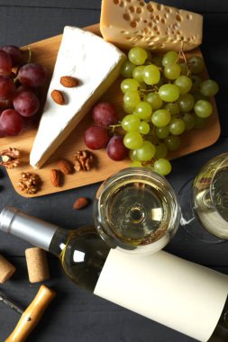 Tahta arka planda çeşitli peynirler, üzümler, fındıklar ve beyaz şarap.