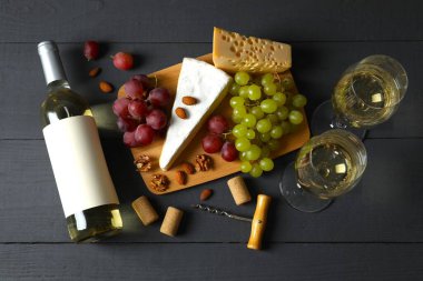 Tahta arka planda çeşitli peynirler, üzümler, fındıklar ve beyaz şarap.