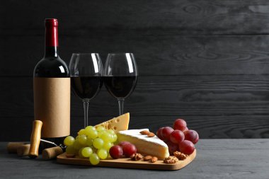 Tahta bir arka planda çeşitli peynirler, üzümler, fındıklar ve kırmızı şarap.