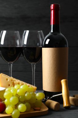 Tahta bir arka planda çeşitli peynirler, üzümler, fındıklar ve kırmızı şarap.