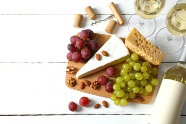 Tahta arka planda çeşitli peynirler, üzümler, fındıklar ve beyaz şarap.