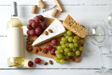 Tahta arka planda çeşitli peynirler, üzümler, fındıklar ve beyaz şarap.
