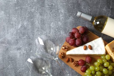 Gri arka planda çeşitli peynirler, üzümler, fındıklar ve beyaz şarap.