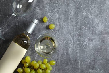 Gri arka planda üzüm ve gözlüklü bir şişe beyaz şarap.