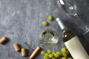 Gri arka planda üzüm ve gözlüklü bir şişe beyaz şarap.