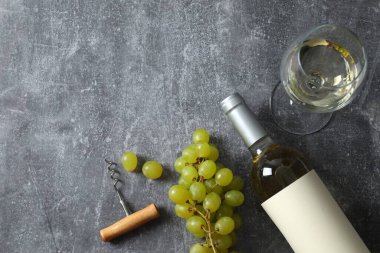 Gri zemin üzerinde üzüm ve cam olan bir şişe beyaz şarap.