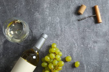 Gri zemin üzerinde üzüm ve cam olan bir şişe beyaz şarap.