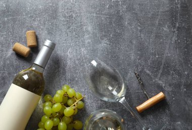Gri arka planda üzüm ve gözlüklü bir şişe beyaz şarap.