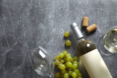 Gri arka planda üzüm ve gözlüklü bir şişe beyaz şarap.