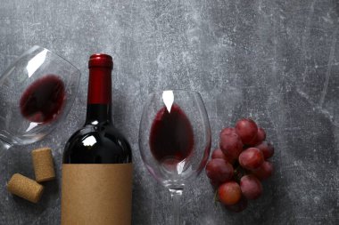 Gri arka planda üzüm ve gözlüklü bir şişe kırmızı şarap.