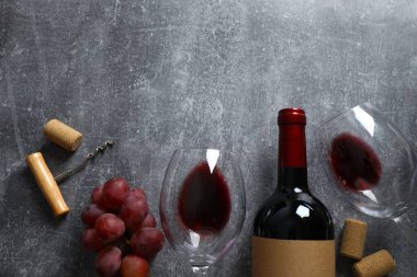 Gri arka planda üzüm ve gözlüklü bir şişe kırmızı şarap.