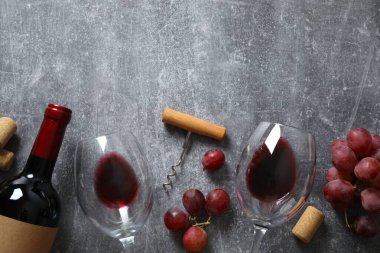 Üzümlü kırmızı şarap, tirbuşon ve gri arka planda gözlük.