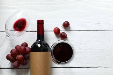 Ahşap zemin üzerinde üzüm ve bardak bulunan bir şişe kırmızı şarap.